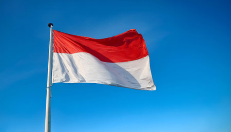 The flag of the Republic of Indonesia flying proudly on a flagpole with a clear sky in the backgroundの写真素材