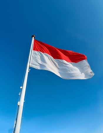 The flag of the Republic of Indonesia flying proudly on a flagpole with a clear sky in the backgroundの写真素材