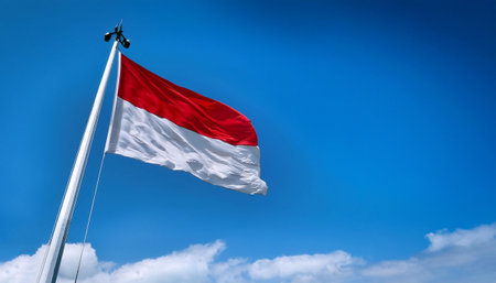 The flag of the Republic of Indonesia flying proudly on a flagpole with a clear sky in the backgroundの写真素材