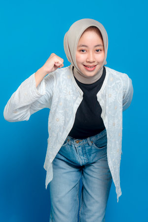 Cheerful young woman wearing hijab smiling confidently while making a dynamic pose with a clenched fist, expressing motivation, determination, and positive energy.の写真素材