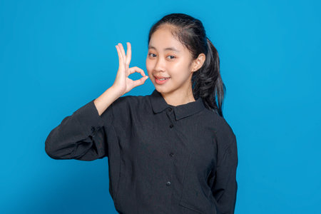 Smiling young Asian girl making an "OK" hand gesture with a confident and friendly facial expression. Perfect image for positive, modern advertising concepts.の写真素材