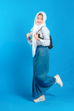 Asian Muslim teenage girl student smiling confidently while carrying backpack and holding pencil, ready to study and learn, education and back to school concept.の写真素材