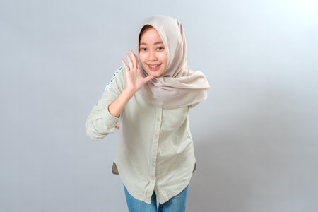 Cheerful young Muslim woman in hijab smiling brightly while cupping her hand near mouth, expressing excitement and enthusiasm. Friendly facial expression ideal for communication themes.の写真素材