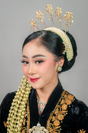 Close-up of a smiling Asian woman in traditional Javanese attire, showing elegance and confidence through expressive eyes, flawless makeup, and intricate golden accessories.の写真素材