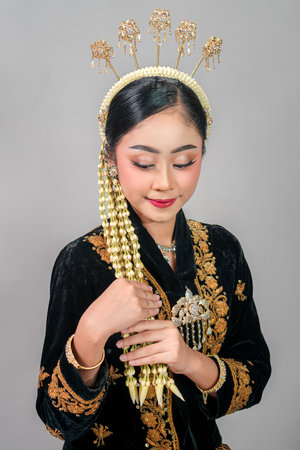 Asian woman in traditional Javanese costume looks down with a serene smile, reflecting grace and inner peace. Her calm facial expression highlights cultural elegance and femininity.の写真素材