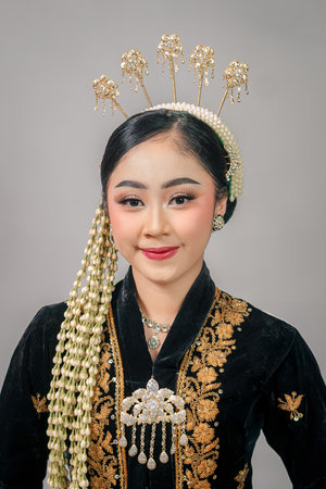 Beautiful Asian woman in traditional Javanese attire smiles softly with elegance, wearing intricate hair accessories and jasmine flowers, showing calm, grace, and timeless beauty.の写真素材