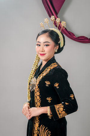 Elegant Asian woman in traditional Javanese attire smiling with confidence and pride, showing calm expression, intricate costume details, and cultural beauty in studio portrait.の写真素材