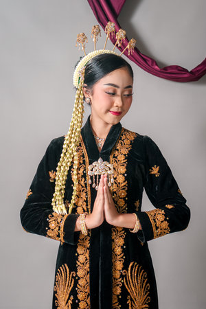 Asian woman in traditional Javanese attire smiling gently with graceful hand gesture. Her serene expression and cultural outfit reflect elegance and heritage proudly.の写真素材