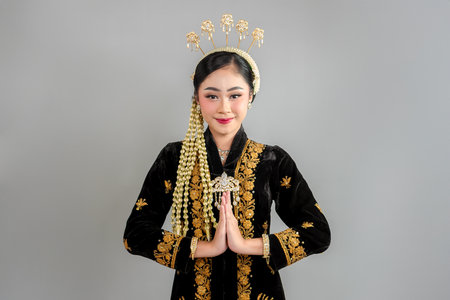 Asian woman in traditional Javanese kebaya smiling gently while making a respectful greeting gesture, showcasing cultural elegance, beauty, and ethnic pride in a graceful pose.の写真素材