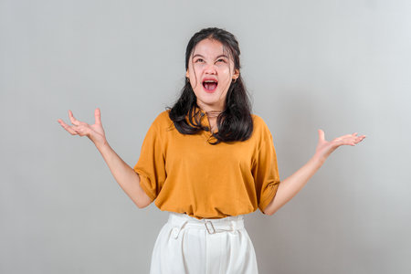 Young Asian woman screaming in anger with wide open mouth and clawed hands, showing intense frustration or rage, expressive face for emotional and dramatic advertising concepts.の写真素材