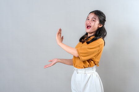 Happy young Asian woman with enthusiastic facial expression showing something to the side. She looks excited and surprised, making her perfect for promotional or advertising themes.の写真素材