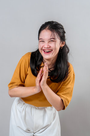 Cheerful young Asian woman laughing joyfully with hands together, showing genuine happiness and a radiant smile. Her expressive face perfectly conveys positivity and spontaneous emotion.の写真素材
