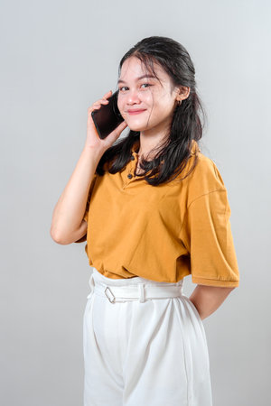 Happy young Asian woman laughing while talking on the phone. Her cheerful expression and genuine joy make this portrait ideal for advertising campaigns about connection and communication.の写真素材