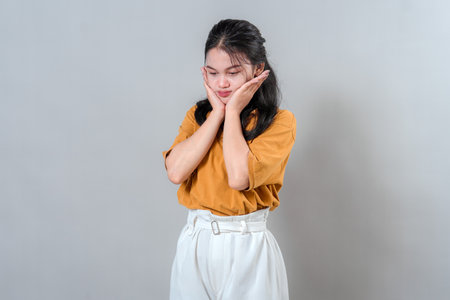 Young woman with sad and disappointed facial expression, resting her face in both hands, looking...