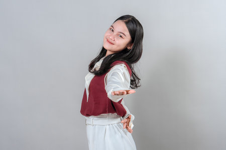 Young woman smiling confidently with an open-arm gesture, expressing warmth, friendliness, and approachability. Perfect for advertising and marketing use.の写真素材