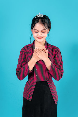 Portrait of a young woman in traditional striped lurik clothing, smiling gently with hands on chest. Subtle expression reflect sincerity, warmth, and confidence.の写真素材