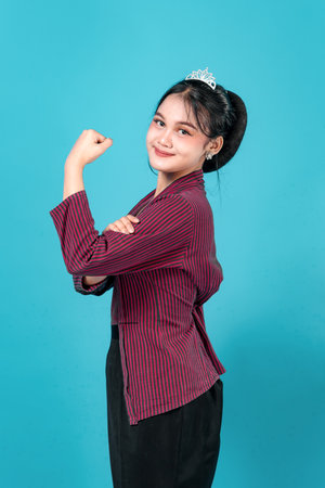 Young Asian woman in traditional attire smiling confidently while showing her bicep, expressing inner strength, charm, and graceful empowerment with elegance.の写真素材