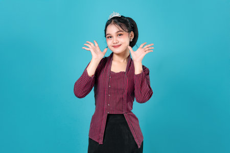 A surprised young Asian woman wearing a striped traditional blouse and black skirt poses against a turquoise background, expressing astonishment with both hands raised.の写真素材