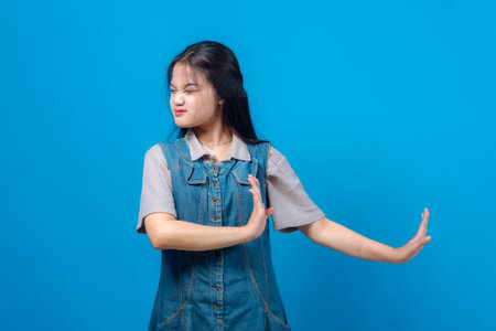 Young Asian woman grimacing and making a firm stop gesture with one hand while crossing the other...