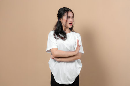 Asian woman crossing arms and showing a stop hand gesture while looking aside with a serious expression. Concept of disagreement, disapproval, or rejection in studio.の写真素材