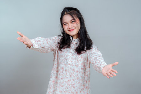Young Asian woman with a warm, inviting smile extending both arms forward as if offering a hug. Expressive face and gentle eyes convey comfort, friendliness, and emotional connection.の写真素材
