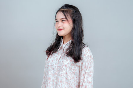 Side profile of a young Asian woman with a calm and gentle smile, looking slightly away, showing a peaceful and confident expression in a bright studio portrait setting.の写真素材
