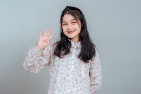 Charming young Asian woman smiles gently while showing four fingers. Her relaxed pose and warm facial expression convey friendliness, approachability, and calm positive energy.の写真素材