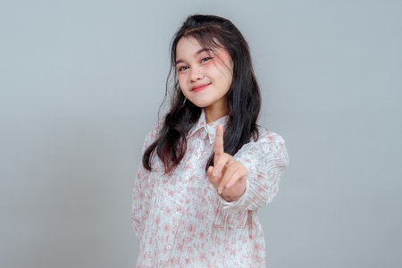Confident young Asian woman smiling gently while raising her index finger, expressing warning or emphasis. Studio portrait ideal for advertising caution, reminder, or advice themes.の写真素材