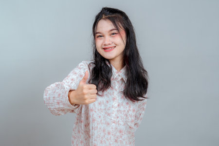 Smiling young Asian woman with braces giving a single thumbs up gesture, expressing approval, positivity, and encouragement with a confident and friendly facial expression.の写真素材