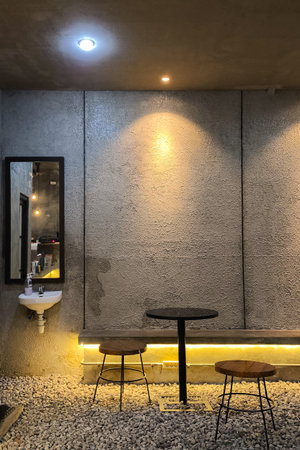 Minimalist industrial background showing a textured concrete wall, round table with two stools,...