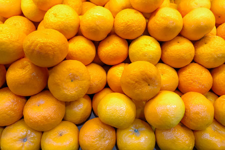 A vibrant pile of fresh mandarin oranges with textured peels displayed in a traditional market....