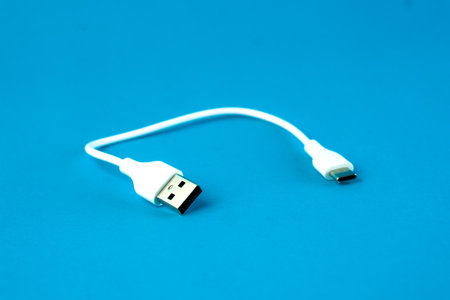 A short white USB to micro-USB cable on a blue background. Ideal for charging and data transfer for smartphones, tablets, and electronic devices. Compact and portable for everyday use.の写真素材