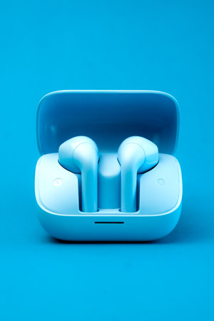 A pair of stylish wireless earbuds inside an open charging case, set against a vibrant blue background. Compact, portable, and modern design, ideal for music lovers and tech enthusiastsの写真素材