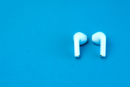 A pair of modern wireless earbuds on a vibrant blue background. Stylish and compact Bluetooth earphones designed for high-quality audio, seamless connectivity, and everyday convenience.の写真素材