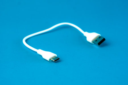 A short white USB to micro-USB cable on a blue background. Ideal for charging and data transfer for smartphones, tablets, and electronic devices. Compact and portable for everyday use.の写真素材
