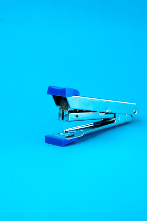 A silver metal stapler with blue plastic accents on a blue background. A compact and durable office...