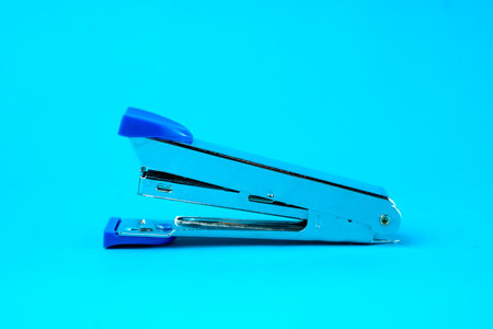 A silver metal stapler with blue plastic accents on a blue background. A compact and durable office tool designed for binding papers efficiently. Ideal for school, office, and home use.の写真素材