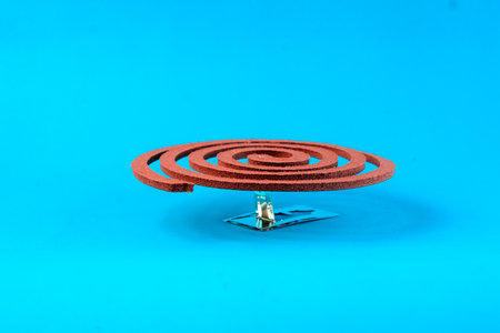 A brown mosquito coil placed on a metal stand against a blue background. Traditional insect repellent used to keep mosquitoes away, ideal for indoor and outdoor protection.の写真素材