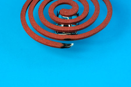 A smoking mosquito coil on a metal stand against a blue background. Traditional insect repellent used to keep mosquitoes away, ideal for indoor and outdoor protection.の写真素材