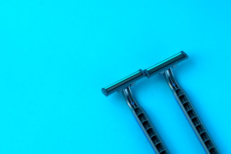 Two disposable razors with black handles on a bright blue background. Minimalist grooming tools for a smooth shave, personal care, and hygiene routine.の写真素材