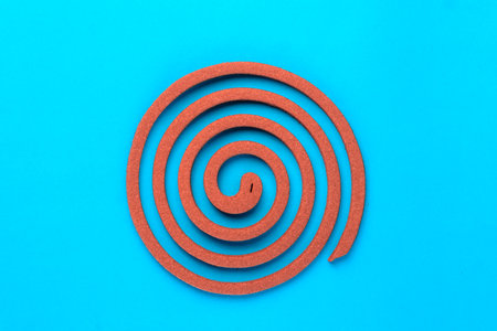 A single brown mosquito coil in a spiral shape on a blue background. Traditional insect repellent used for mosquito control, providing protection for indoor and outdoor environments.の写真素材