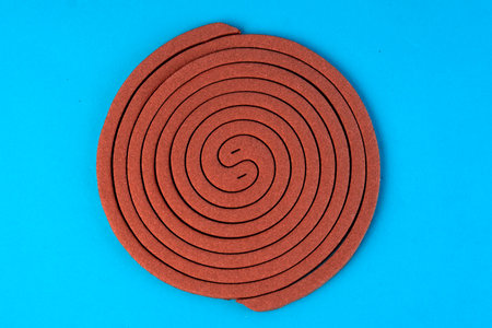 A brown mosquito coil in a spiral shape on a blue background. Insect repellent for outdoor and indoor use, designed to keep mosquitoes away and provide protection from bites.の写真素材