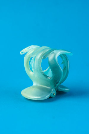 A translucent plastic hair claw clip with a spring mechanism on a bright blue background. The close-up shot highlights its curved design, ideal for securing hair in place stylishly.の写真素材