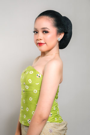 A young Indonesian woman in a green traditional outfit, smiling gently and confidently, with a...