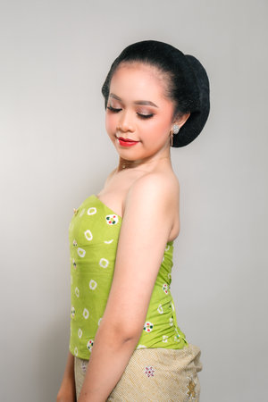 A young Indonesian woman in a green traditional outfit, smiling gently and confidently, with a...