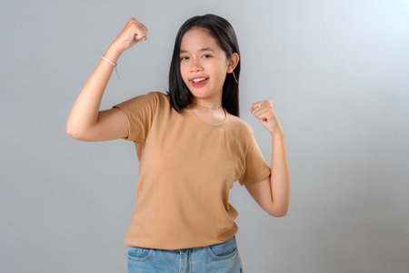 Portrait of a confident young Asian woman smiling proudly and showing her biceps in a power pose,...