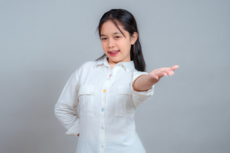 Confident young Asian woman with inviting facial expression and extended arm gesture, looking directly at the camera, suggesting a welcoming, persuasive, or promotional message.の写真素材