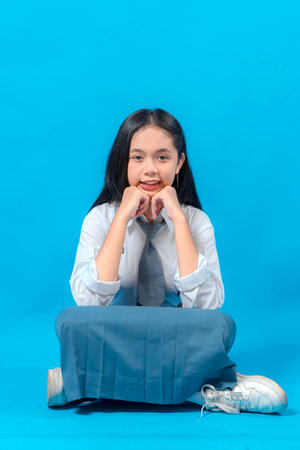 Indonesian high school girl sitting on the floor, resting her chin on her hands with a sweet and confident smile. Her facial expression conveys positivity and youthful charm.の写真素材
