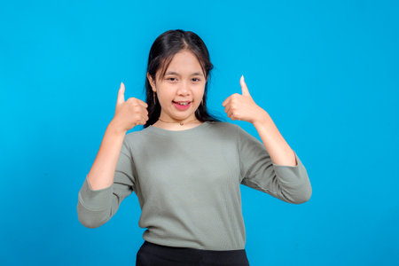 Happy young Asian woman smiling confidently and showing double thumbs up gesture. Her bright and...