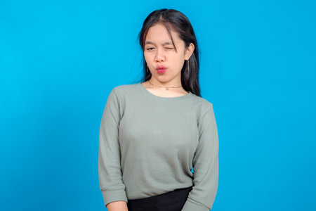 Portrait of a young Asian woman with long black hair winking and pouting playfully against a blue background. Fun, flirty, and expressive facial gesture concept.の写真素材